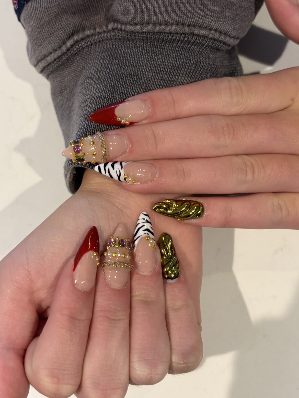 Red and gold chrome nails with jewel accents